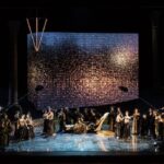 Rappresentazione dell'opera Aida al Circo Massimo, con il cast sul palco davanti a una grande scenografia luminosa.