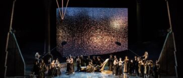 Rappresentazione dell'opera Aida al Circo Massimo, con il cast sul palco davanti a una grande scenografia luminosa.