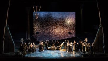 Rappresentazione dell'opera Aida al Circo Massimo, con il cast sul palco davanti a una grande scenografia luminosa.