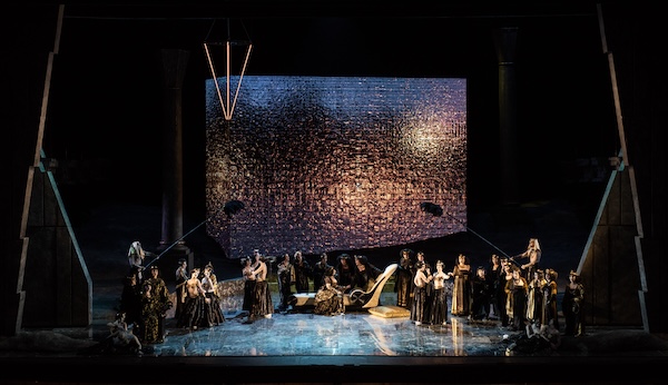 Rappresentazione dell'opera Aida al Circo Massimo, con il cast sul palco davanti a una grande scenografia luminosa.