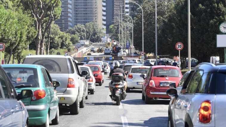 Traffico intenso su una strada di Roma, con auto e scooter in coda vicino a un'area interessata da lavori e modifiche alla viabilità.