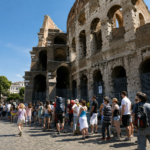 Turisti in fila davanti al Colosseo a Roma durante una giornata estiva, sotto il sole e con temperature elevate.
