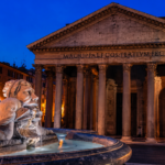 Vista serale del Pantheon di Roma illuminato, con la Fontana del Pantheon in primo piano e il cielo blu intenso sullo sfondo.