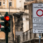 Segnale della Ztl di Roma con controllo elettronico degli accessi e semaforo rosso, sullo sfondo edifici e resti storici del centro della Capitale.