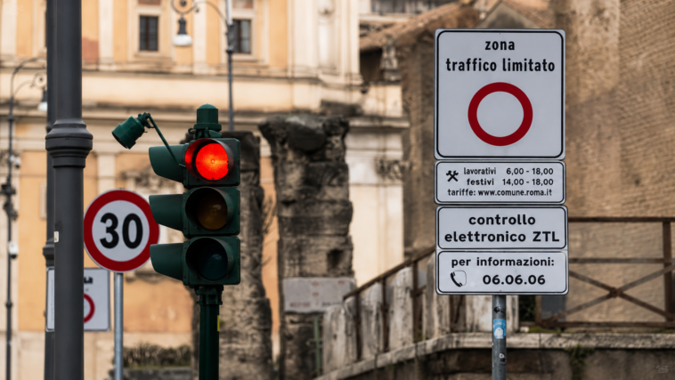 Segnale della Ztl di Roma con controllo elettronico degli accessi e semaforo rosso, sullo sfondo edifici e resti storici del centro della Capitale.