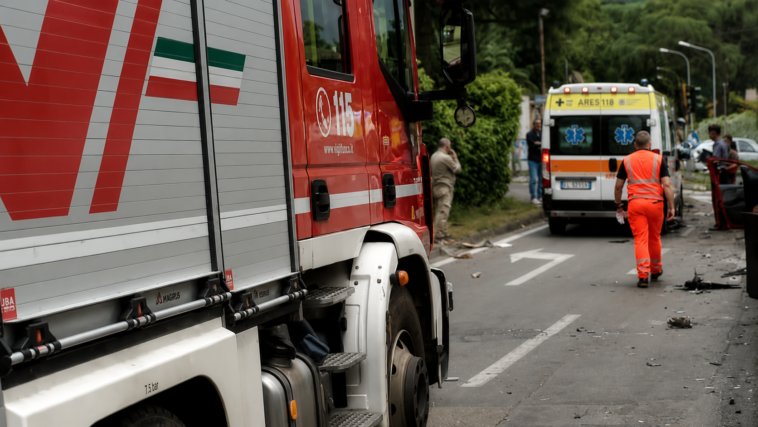 Mezzi di soccorso e ambulanza lungo una strada dopo un incidente, con detriti presenti sulla carreggiata.