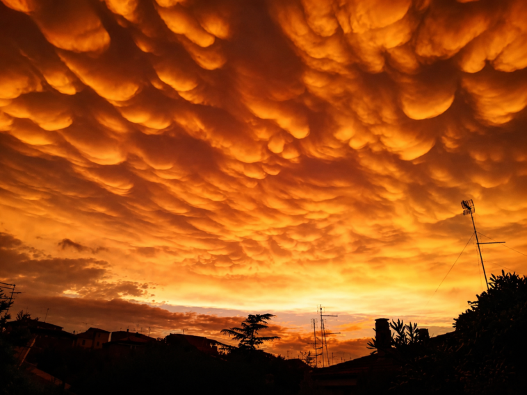 Cielo di Roma illuminato da intense tonalità arancioni e gialle, con particolari formazioni nuvolose sopra i tetti della città.