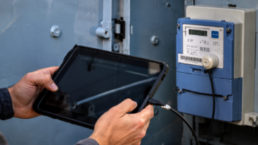 Tecnico controlla un contatore elettrico digitale con un tablet durante un intervento sulla rete elettrica.