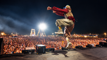 Jovanotti salta sul palco durante un concerto davanti a una grande folla illuminata dalle luci dello spettacolo.