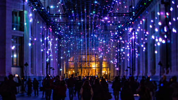 Installazione luminosa immersiva con punti di luce colorati e visitatori all’interno di uno spazio espositivo.