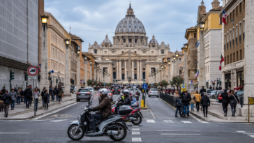 Traffico nel centro di Roma con auto e scooter in circolazione e la Basilica di San Pietro sullo sfondo.