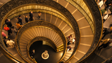 Scala a chiocciola monumentale vista dall’alto con numerosi visitatori all’interno di un museo.