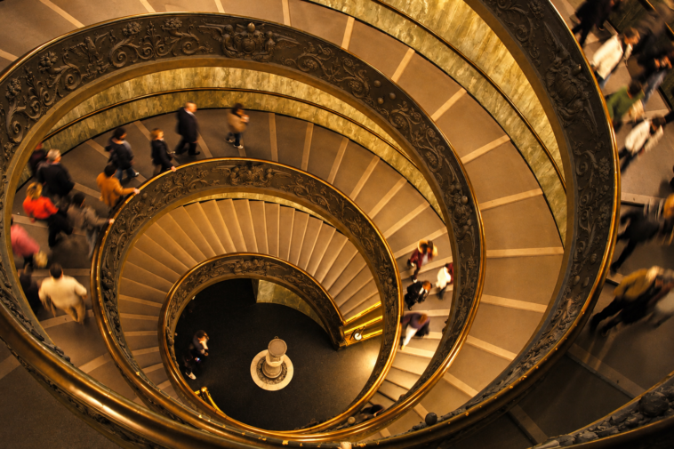 Scala a chiocciola monumentale vista dall’alto con numerosi visitatori all’interno di un museo.