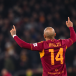 Calciatore della Roma con la maglia numero 14 visto di spalle durante una partita, con le braccia alzate.
