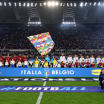Nazionali di Italia e Belgio schierate sul campo dello Stadio Olimpico prima di una partita, con gli spalti pieni di tifosi.