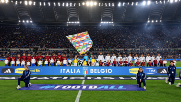 Nazionali di Italia e Belgio schierate sul campo dello Stadio Olimpico prima di una partita, con gli spalti pieni di tifosi.