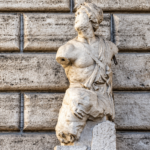 Statua antica in marmo di Pasquino, priva delle braccia, davanti alla facciata in pietra di Palazzo Braschi a Roma.