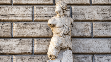 Statua antica in marmo di Pasquino, priva delle braccia, davanti alla facciata in pietra di Palazzo Braschi a Roma.