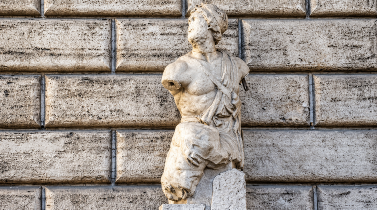 Statua antica in marmo di Pasquino, priva delle braccia, davanti alla facciata in pietra di Palazzo Braschi a Roma.