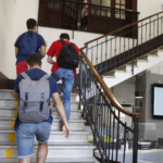 Studenti con zaini salgono le scale all’interno di un istituto scolastico.