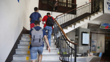 Studenti con zaini salgono le scale all’interno di un istituto scolastico.