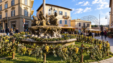 Piazza di un borgo del Lazio decorata con grappoli d’uva e rami verdi intorno a una fontana, durante una festa autunnale.