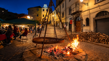 Festa serale in un borgo del Lazio con grande falò, braciere sospeso e stand gastronomici nel centro storico.