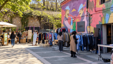 Mercatino all'aperto con stand di artigianato e abbigliamento vintage, visitatori tra gli espositori e un edificio decorato con murales colorati e insegna Teatro.